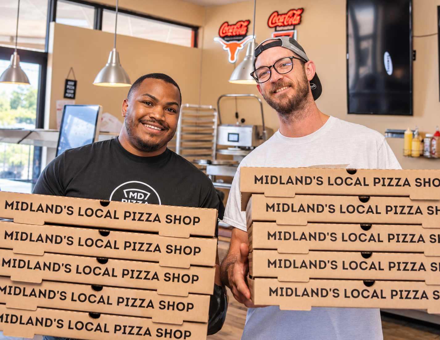 Dru and a teammate holding stacks of Midland's Local Pizza Shop boxes